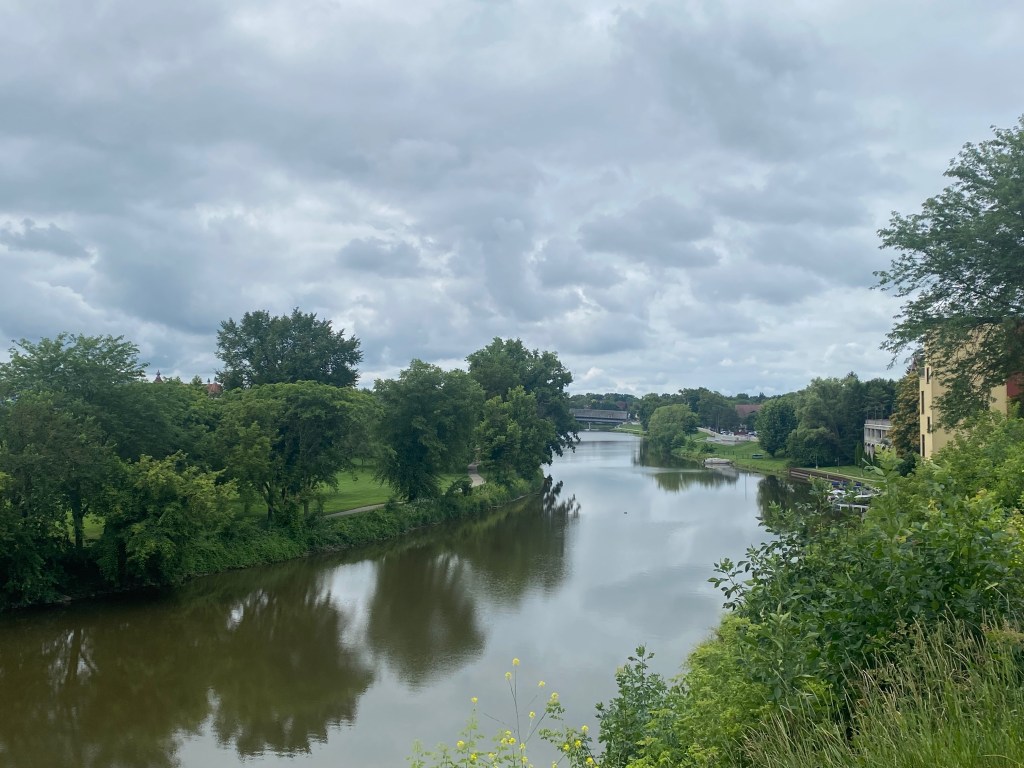 A river winds between two curving tree-lined banks, with a few buildings visible on the right.
