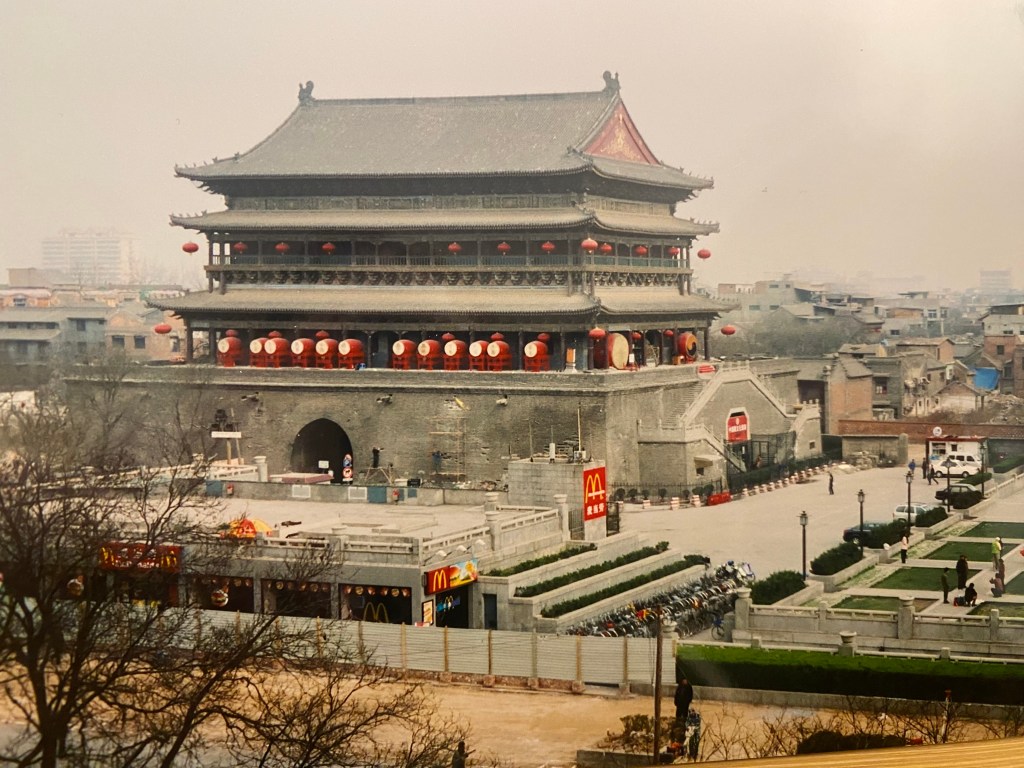 A large Chinese-style gate stands in the center of a massive intersection, with a McDonald's in the foreground.