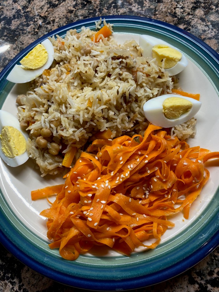 A plate holds a shaved carrot salad and a serving of rice pilaf, with hard-boiled eggs on the side.