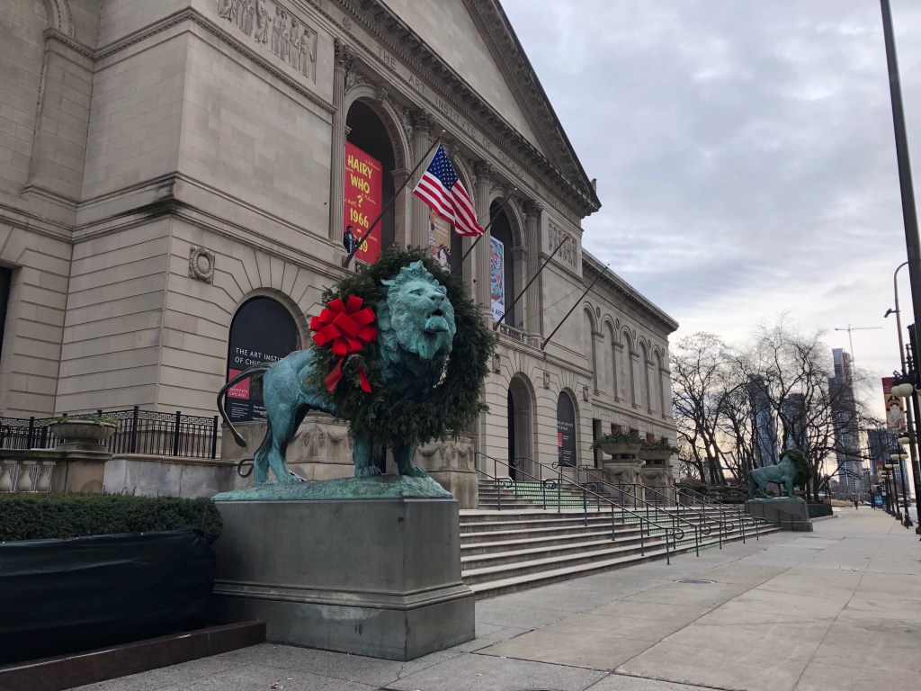 Exterior of the Art Institute of Chicago, with a green wreath and red bow hanging around the neck of one lion in front of the building.