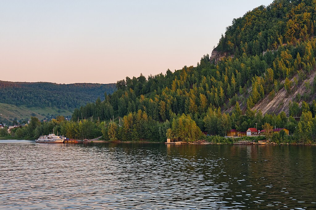 A wide-angle view of the Volga River, with small houses visible among trees in the distance.
