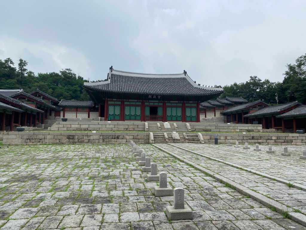 A wide-angle photograph of Gyeunghuigung Palace in Seoul, a traditional Korean building complex with a large stone courtyard in front.
