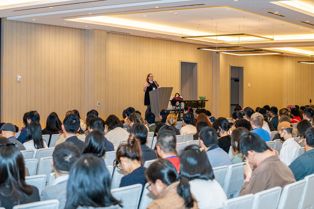 Maura Cunningham stands at a lectern in front of a large audience.