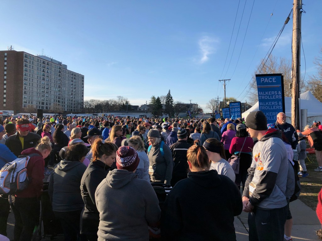A large crowd of people stand in a race corral waiting for a 5K to start.