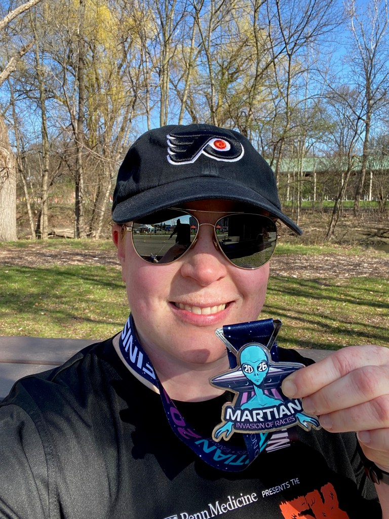 A woman wearing a Philadelphia Flyers baseball cap holds up a race medal 