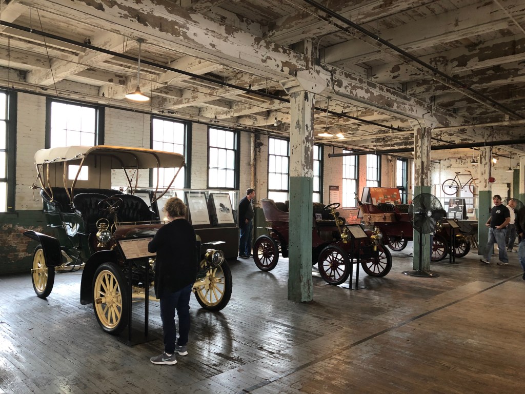 Inside an old factory building, with wooden floors and peeling paint on the ceiling, sit several early Ford Model Ts.