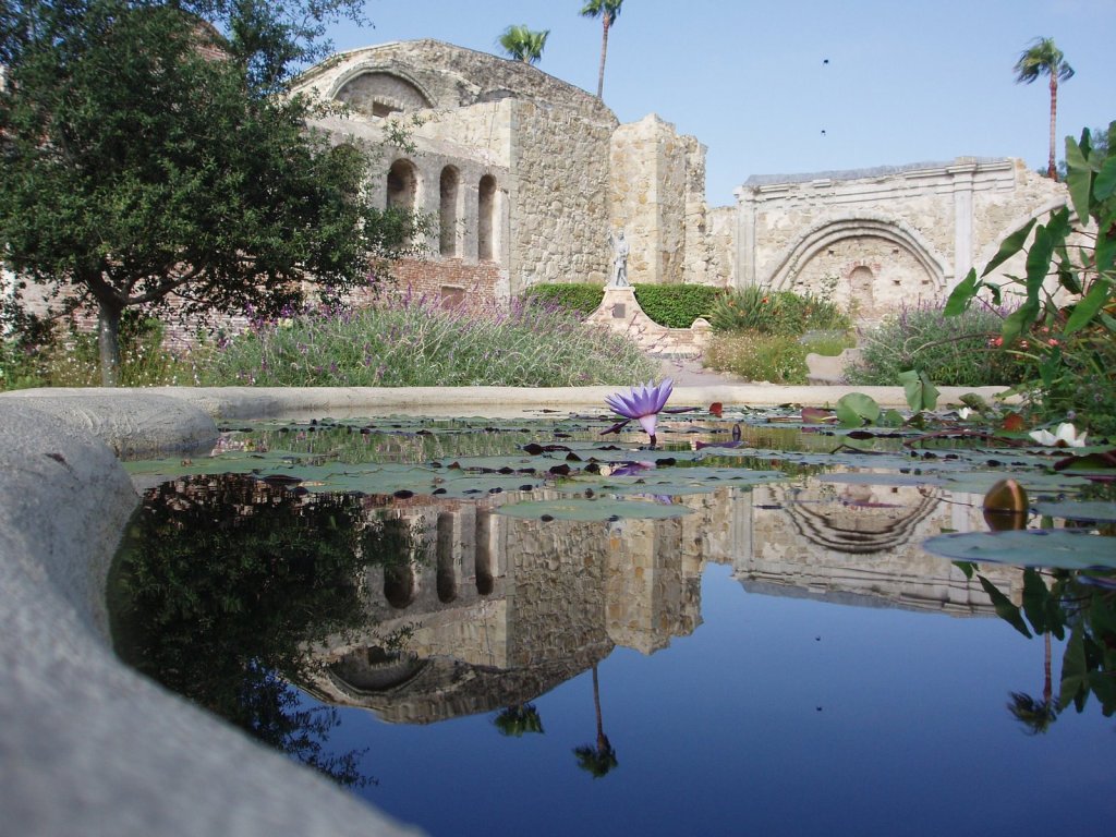 In the background is an old stone church. In the foreground, a pool filled with water reflects the image of the church.